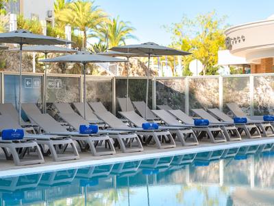Área de piscina del hotel con tumbonas, sombrillas y palmeras.