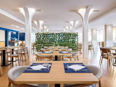 Un restaurante moderno y luminoso con muebles de madera y plantas verdes, ideal para huéspedes del hotel.