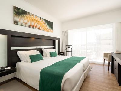 Habitación de hotel moderna con cama doble, ropa de cama verde, escritorio y luz brillante del balcón.
