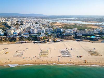 Amplia playa de arena con zonas marcadas frente a una ciudad costera urbana y montañas al fondo.