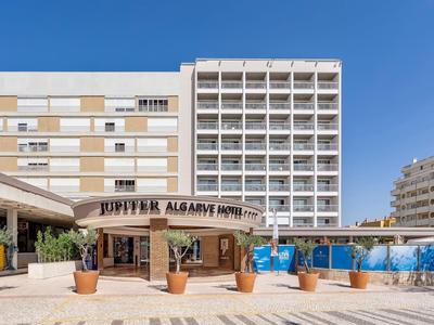 Complejo hotelero moderno con edificio de varios pisos, piscina y terraza soleada bajo cielo despejado.