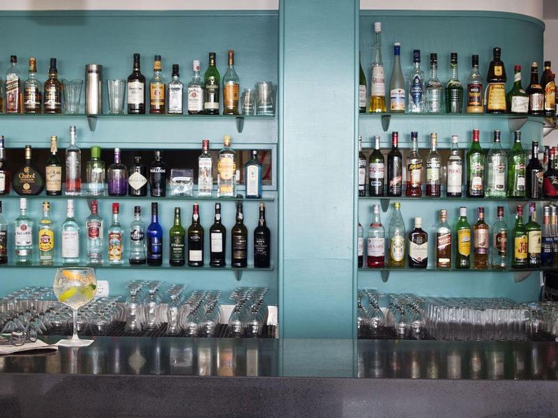 Moderne hotelbar met diverse drankflessen op glazen planken en toonbank met drankjes.
