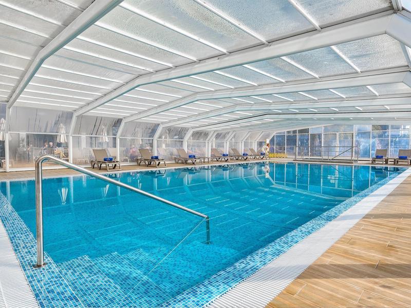 Overdekt zwembad met helder water, houten dek en glazen wanden die daglicht doorlaten.