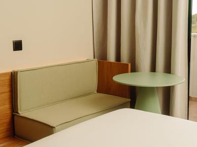 Kleines Hotelzimmer mit grünem Sofa, rundem Tisch und Blick auf Balkon.