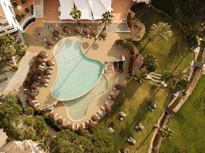 Luftaufnahme eines Hotels mit einem Pool in Herzform und einem Sonnenbereich, umgeben von grünen Gärten.