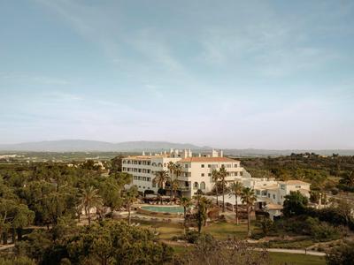 Ein Hotelkomplex umgeben von viel Grün und Bäumen unter einem klaren Himmel.