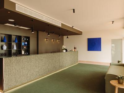 Moderner Hotellobby-Empfang mit grauer Rezeption, grünem Teppich und blauem Kunstwerk.