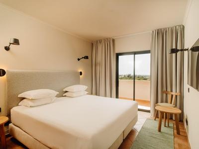 Hell eingerichtetes Hotelzimmer mit Doppelbett, Balkon und TV an der Wand.