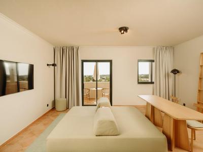 Modern eingerichtetes Hotelzimmer mit Doppelbett, Fernseher und Blick auf Terrasse.