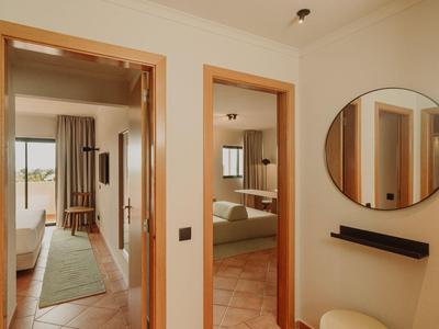 Flur mit zwei offenen Türen zu hellen, modern eingerichteten Hotelzimmern und rundem Spiegel an der Wand.