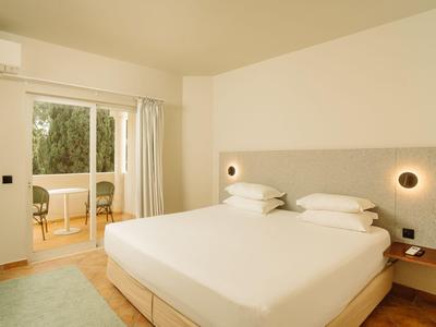 Modernes Hotelzimmer mit großem Bett und Balkon mit Blick ins Grüne.