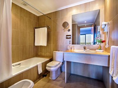 Hotel bathroom with bathtub, toilet, large mirror, and wooden wall panels, bright and clean.