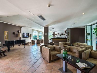 Spacious hotel lobby with plush seating, tiled floor, a grand piano, and natural light from large windows.