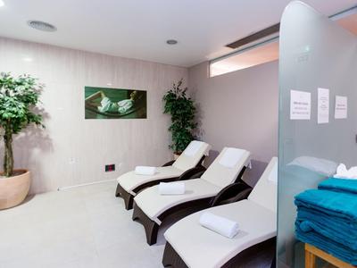 Spa room with three lounge chairs, towels, plants, and calming wall art in soft lighting.