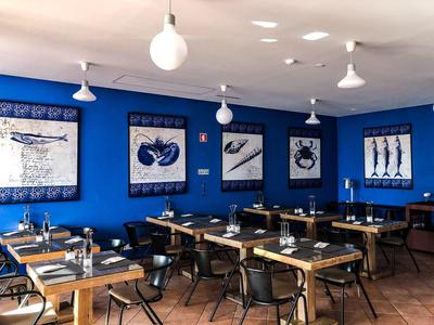Dining area with wooden tables, black chairs, blue walls, and seafood-themed artwork under white pendant lights.