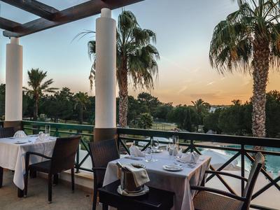 Gemütlicher Terrassenbereich mit gedeckten Tischen und Blick auf Palmen bei Sonnenuntergang.