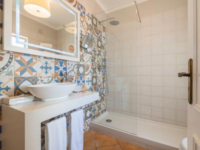 Bathroom with patterned tile wall, walk-in shower, white countertop, and round mirror.