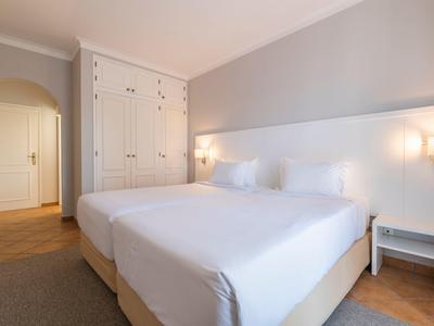 Bright hotel room with double bed, white walls, wooden floor, and built-in wardrobe.
