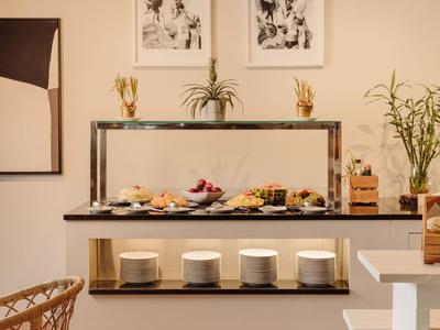 Buffet mit verschiedenen Speisen, Pflanzen und moderner Wanddekoration in einem hellen Raum.