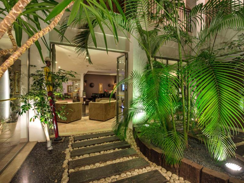 Cozy outdoor patio with lush green plants and wicker seating near a hotel entrance.