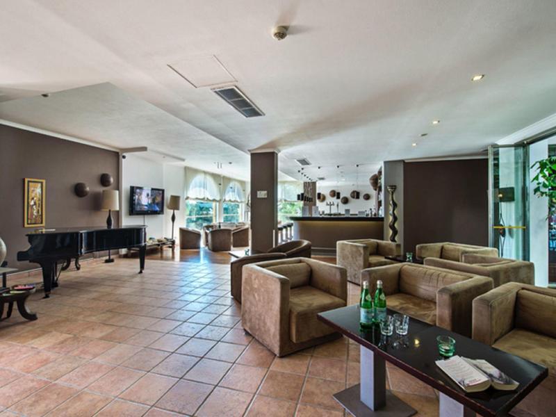 Spacious hotel lobby with plush seating, tiled floor, a grand piano, and natural light from large windows.