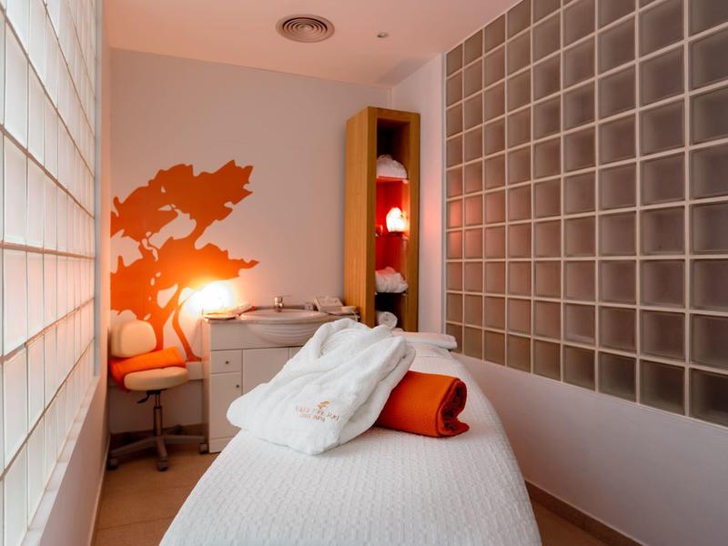 Cozy massage room with white towel-covered table, orange bolster, warm lighting, and decorative wall art.