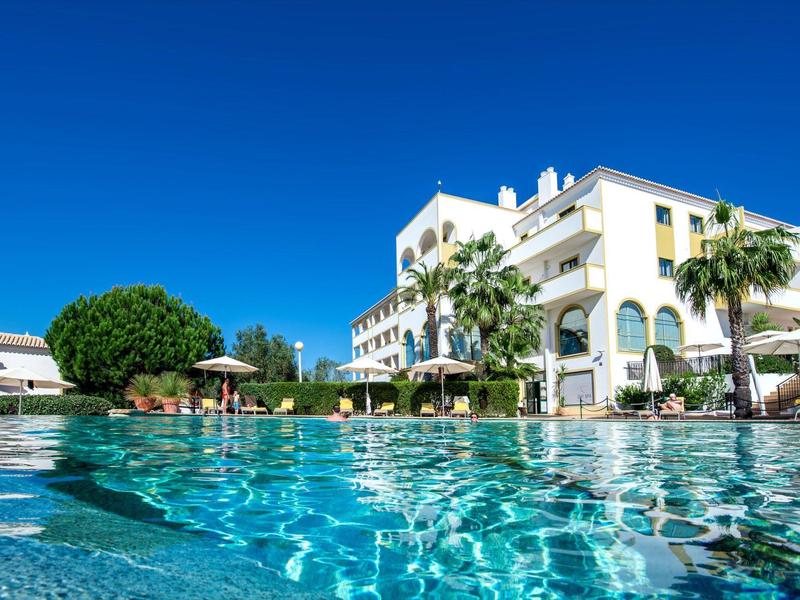 Luxurious hotel with clear swimming pool, palm trees, and blue sky in a tropical setting.