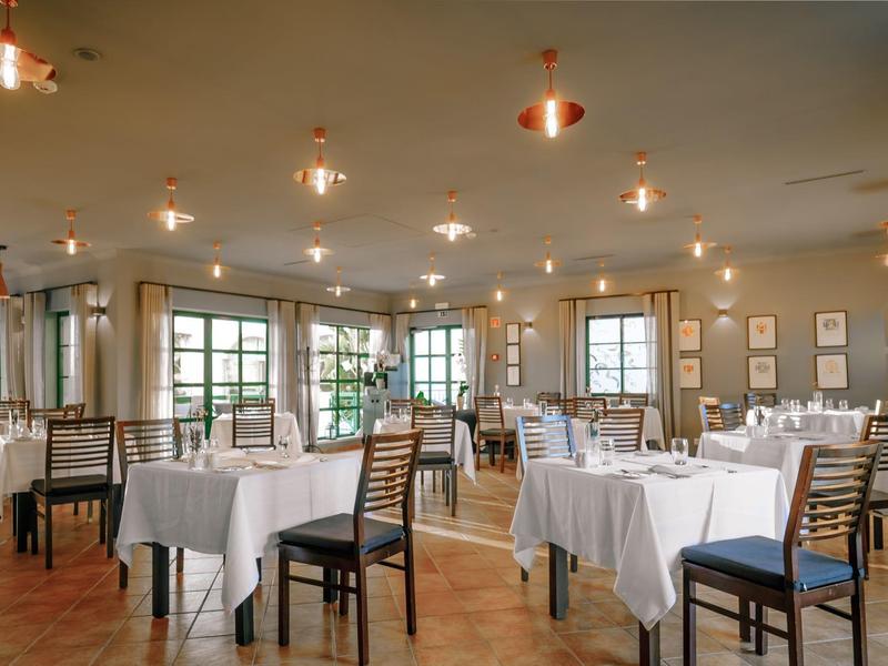 Spacious hotel restaurant with wooden chairs, white tablecloths, and warm lighting.