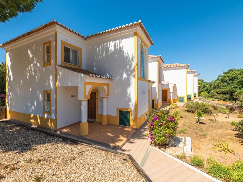 White two-story house with tiled roof under a clear blue sky, surrounded by dry landscape and greenery.