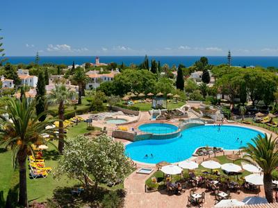 Blick auf einen Hotelpool mit Sonnenliegen, Palmen und Meer im Hintergrund.