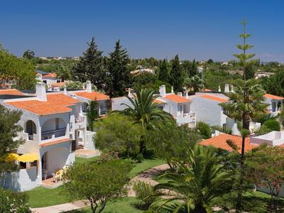 Case vacanze bianche con tetti rossi in un giardino verde sotto un cielo azzurro.