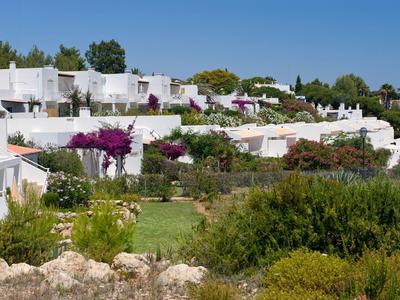 Case bianche con terrazze e fiori in un giardino verde sotto un cielo soleggiato.