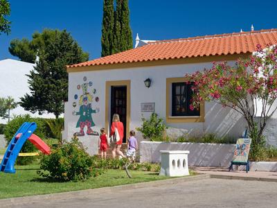 Piccola casa vacanze bianca con tetti rossi e un'area giochi in giardino.