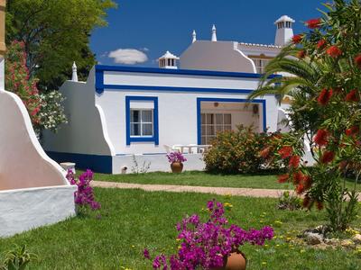 Casa bianca con telai delle finestre blu, circondata da prato verde e piante fiorite.
