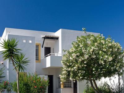 Edificio alberghiero bianco moderno con balconi e piante mediterranee sotto un cielo limpido.