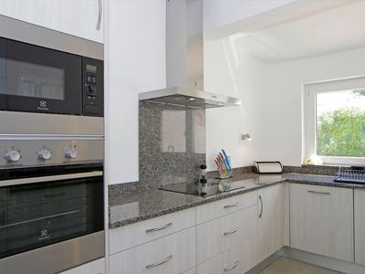 Cucina moderna e luminosa con mobili bianchi, forno, microonde e finestra con vista sul verde.