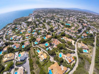 Vista aerea di una città costiera con numerose case e diverse piscine.