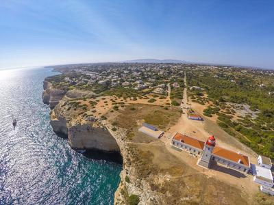 Vista aerea di una scogliera costiera con un faro e il mare sotto un cielo sereno.