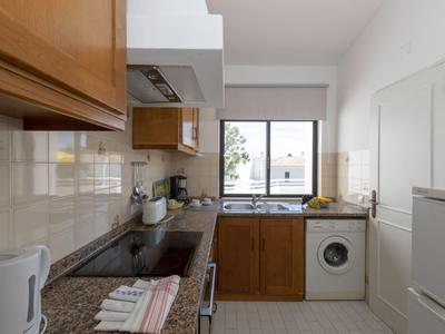 Piccola cucina con mobili in legno, lavatrice e finestra con vista esterna.