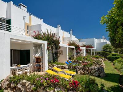 Weiße Ferienwohnungen mit gelben Liegestühlen und Blumen unter blauem Himmel