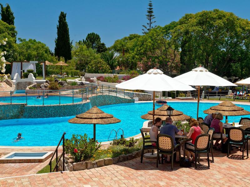 Vista di una piscina dell'hotel con ombrelloni, sedie e ospiti in una giornata di sole.