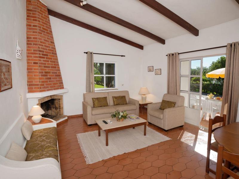 Soggiorno luminoso con camino, divano, poltrone e accesso diretto alla terrazza con ombrellone.