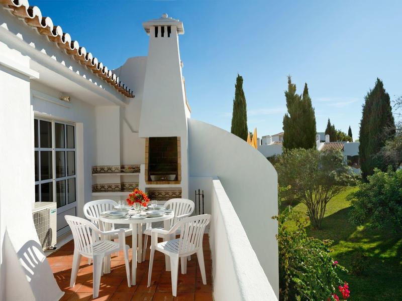 Balcone con tavolo bianco, sedie e barbecue, cielo soleggiato su paesaggio verde.