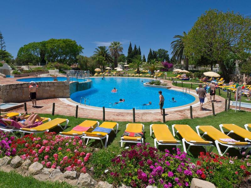 Piscina rotonda all'aperto con lettini gialli e fiori colorati in un giardino dell'hotel.
