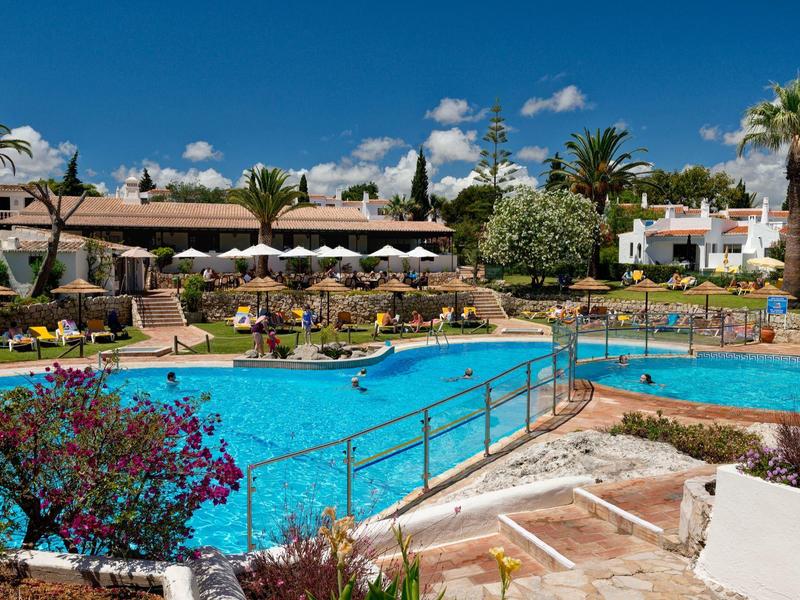 Grande piscina dell'hotel con lettini, ombrelloni e palme in una giornata di sole.