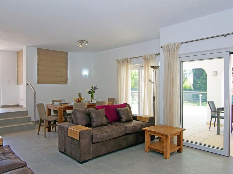 Zona giorno luminosa con divano marrone, tavolo in legno e accesso alla terrazza tramite porte scorrevoli.