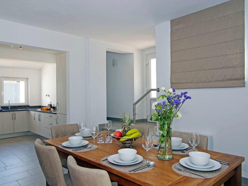 Zona pranzo con tavolo in legno apparecchiato e vista su cucina moderna.