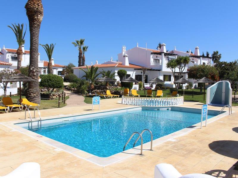 Una piscina all'aperto limpida circondata da palme e case bianche sotto un cielo soleggiato.