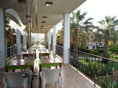 Balcony with tables and chairs next to a garden with palm trees at a hotel.
