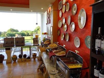 Breakfast buffet with hot dishes in front of a red wall decorated with plates in a bright room.